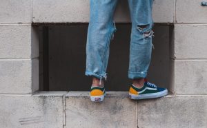 A pair of lower legs in torn jeans and tennis shoes with no socks standing on a window ledge.